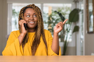 African american woman using smartphone very happy pointing with hand and finger to the side