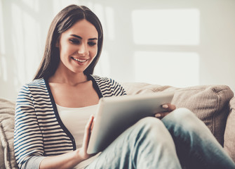 Young Smiling Woman Watchung into Tablet at Home