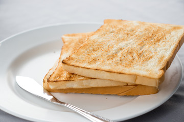 Stack of toasted bread with butter knife on white dish background