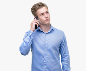 Young handsome blond man using smartphone serious face thinking about question, very confused idea
