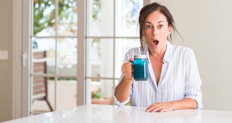 Middle aged woman drinking milk shake in a glass scared in shock with a surprise face, afraid and excited with fear expression