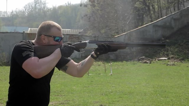 A man in glasses targets and shoots with a double-barreled rifle. Slowmotion
