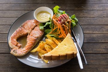 Salmon steak with french fried, bread and vegetable in dish on wooden table