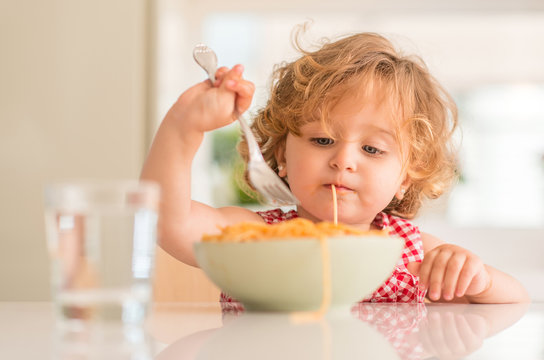 Beautiful blond child eating spaghetti with fork at home