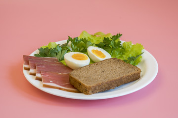 breakfast. Boiled eggs, bacon, greens in a white plate on pink background