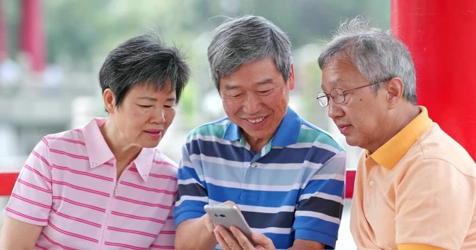 Senior friends talk together look at mobile phone at outdoor park
