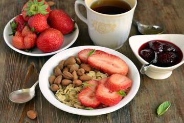 Oatmeal porridge, fresh strawberries, almonds and jam for breakfast