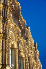 The building is lit at night with garlands and lights. 