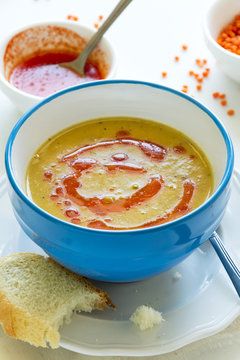 Red lentil soup with chili pepper sauce and bread on white wooden table