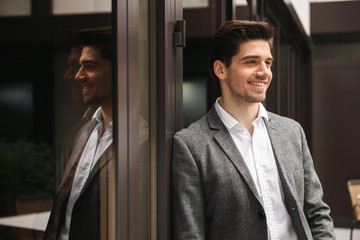 Smiling young businessman standing at the glass doors