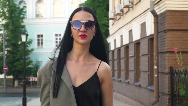 Stylish and confident woman in sunglasses walking at urban street, slow motion