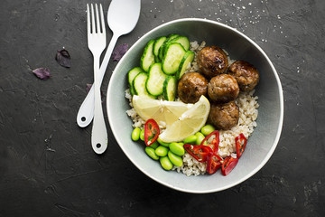 Baked teriyaki meatballs with brown rice, cucumbers, hot pepper, lemon slices in a bowl. Top View