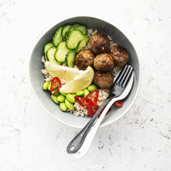Baked teriyaki meatballs with brown rice, cucumbers, hot pepper, lemon slices in a bowl. Top View