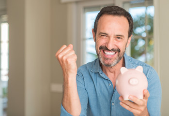 Middle age man save money on piggy bank screaming proud and celebrating victory and success very...