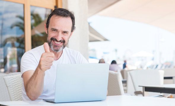 Handsome senior man using laptop at restaurant happy with big smile doing ok sign, thumb up with fingers, excellent sign