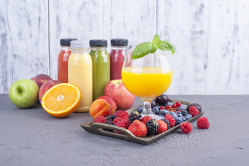 Juice in bottles, different and in a glass. Assorted berries and fruits. Gray background. Detox food. Copy space.