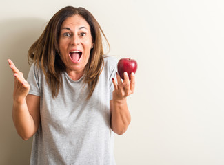 Middle age woman holding a green apple very happy and excited, winner expression celebrating victory screaming with big smile and raised hands