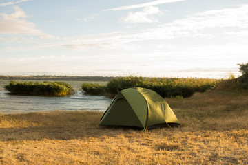 Green tent of hikers near river during the sunset or sunrise