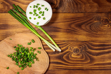 Sour cream and green onion on wooden table. Top view