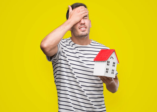Handsome real estate agent holding a house stressed with hand on head, shocked with shame and surprise face, angry and frustrated. Fear and upset for mistake.