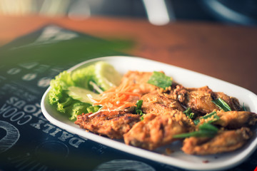 Thai style fried chicken wings on a round white plate on a wood table
