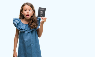 Fototapeta premium Brunette hispanic girl holding passport of United States of America scared in shock with a surprise face, afraid and excited with fear expression