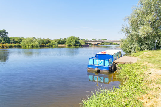Pleasure boats moored on the banks of the calm River Trent at Gunthorpe Bridge on a cloudless summer morning.