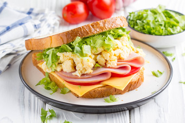 Ham sandwich with scrambled egg, cheese, tomato, lettuce, tasty healthy Breakfast on white wooden background