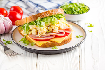 Ham sandwich with scrambled egg, cheese, tomato, lettuce, tasty healthy Breakfast on white wooden background