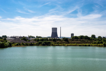 A huge chimney of a nuclear power plant in western Germany, a turquoise water reservoir, a blue sky with white clouds.
