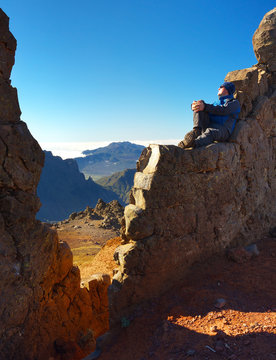 Resting man sitting on the rocky wall above the crater Caldera de Taburiente, Island of La Palma, Canary Islands, Spain