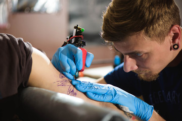 Master tattoo draws the black paint on the clients tattoo. Tattoo artist holding a tattoo machine...