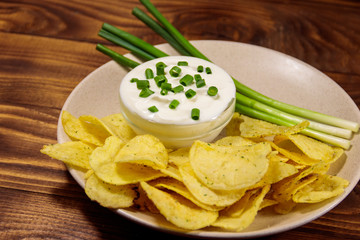 Crispy potato chips with green onion and sour cream on wooden table