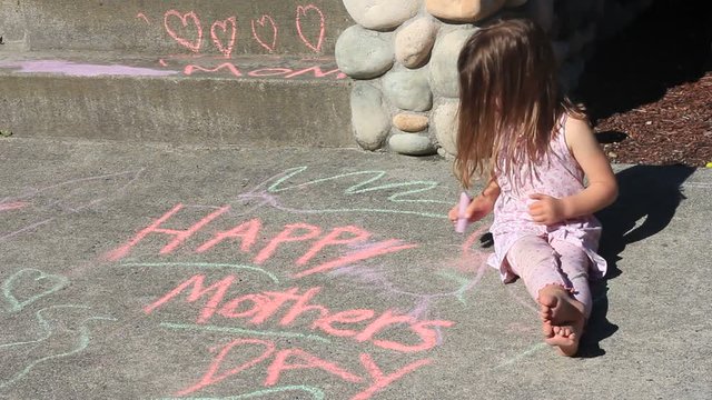 Little Girl With Messy Hair And Her Pj's Still On Writing Happy Mothers Day On The Driveway Outside Her House.