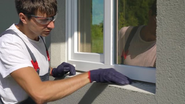 Closeup worker in safety glasses cleaning surface for metal sill installation. Builder preparing workplace for assembling PVC window construction outside building. Technology, exterior design concept
