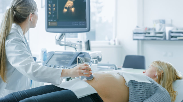 In the Hospital, Pregnant Woman Getting Sonogram / Ultrasound Screening / Scan, Obstetrician Checks Picture of the Healthy Baby on the Computer Screen. Happy Future Mother Talks with Doctor.