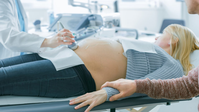 In the Hospital, Close-up Shot of the Doctor Performs Ultrasound / Sonogram Procedure, Pregnant Female Lying on the Bed. Obstetrician Moving Transducer on the Belly of the Future Mother.
