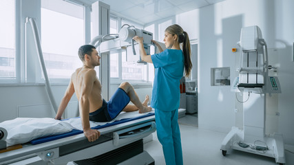 In the Hospital, Man Sitting on a Bed, Female Technician adjusts X-Ray Machine for Scanning His Leg...