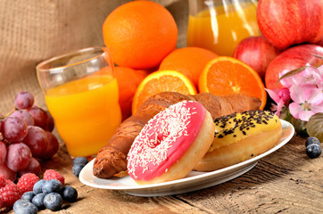 Donuts, croissant, orange juice, blueberries, raspberries, apples - sweet breakfast on wooden table