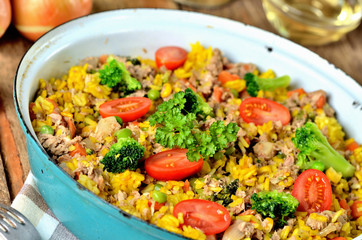 Close-up of tuna risotto with vegetables, tomatoes, broccoli and parsley in the old pan, onions, cans and oil in the background