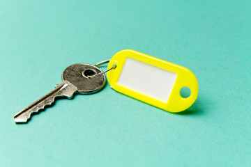 Yellow key tag on a turquoise textured cardboard background.The concept of rent, selling. Template. Trend colors