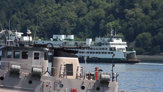 A passenger and vehicle ferry passes by a coast guard vessel that's at port.