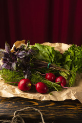 Bunches of fresh herbs of parsley, dill, basil, radish and sorrel lie on a plate covered a wrapping paper an old wooden table
