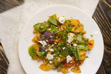 Pasta with green peas, herbs and seasonings, cherry tomatoes in a white plate on a white napkin on an old wooden table. Copy space.
