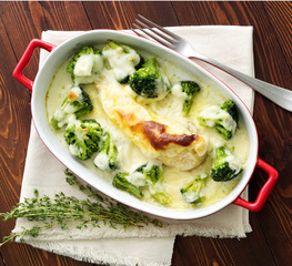 Chicken fillet baked with broccoli in bechamel sauce on dark wooden table. Healthy food, clean eating, top view.