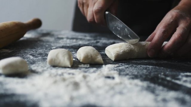 Slow motion of female cook hands cut the dough into pieces with a kitchen knife