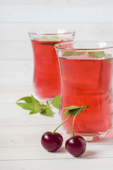 Cherry juice with mint leaves and fresh cherries on a white wooden table