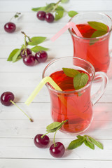 Cherry juice with mint leaves and fresh cherries on a white wooden table