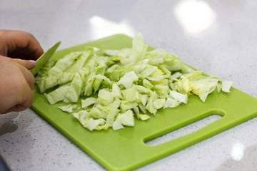 Hands cut a lettuce salad with a knife on a green board
