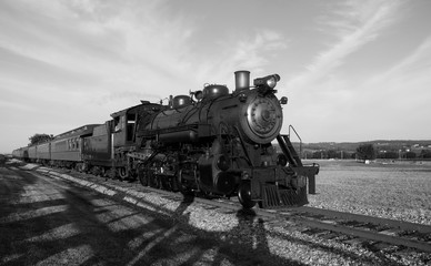 Steam train on tracks coming at you in black and white
